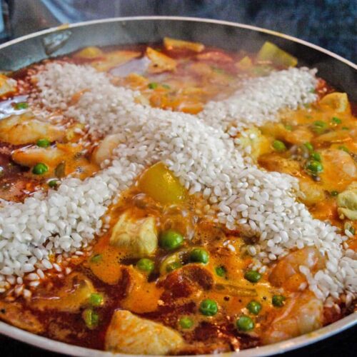 Paella with rice added in a cross
