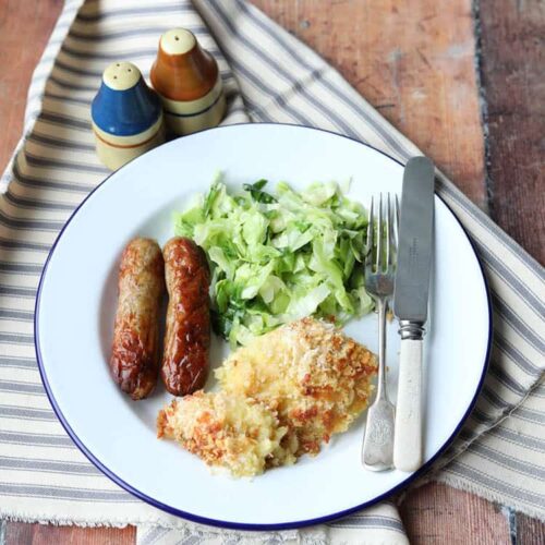 plate of cheesy parsnip gratin with sausages and cabbage.