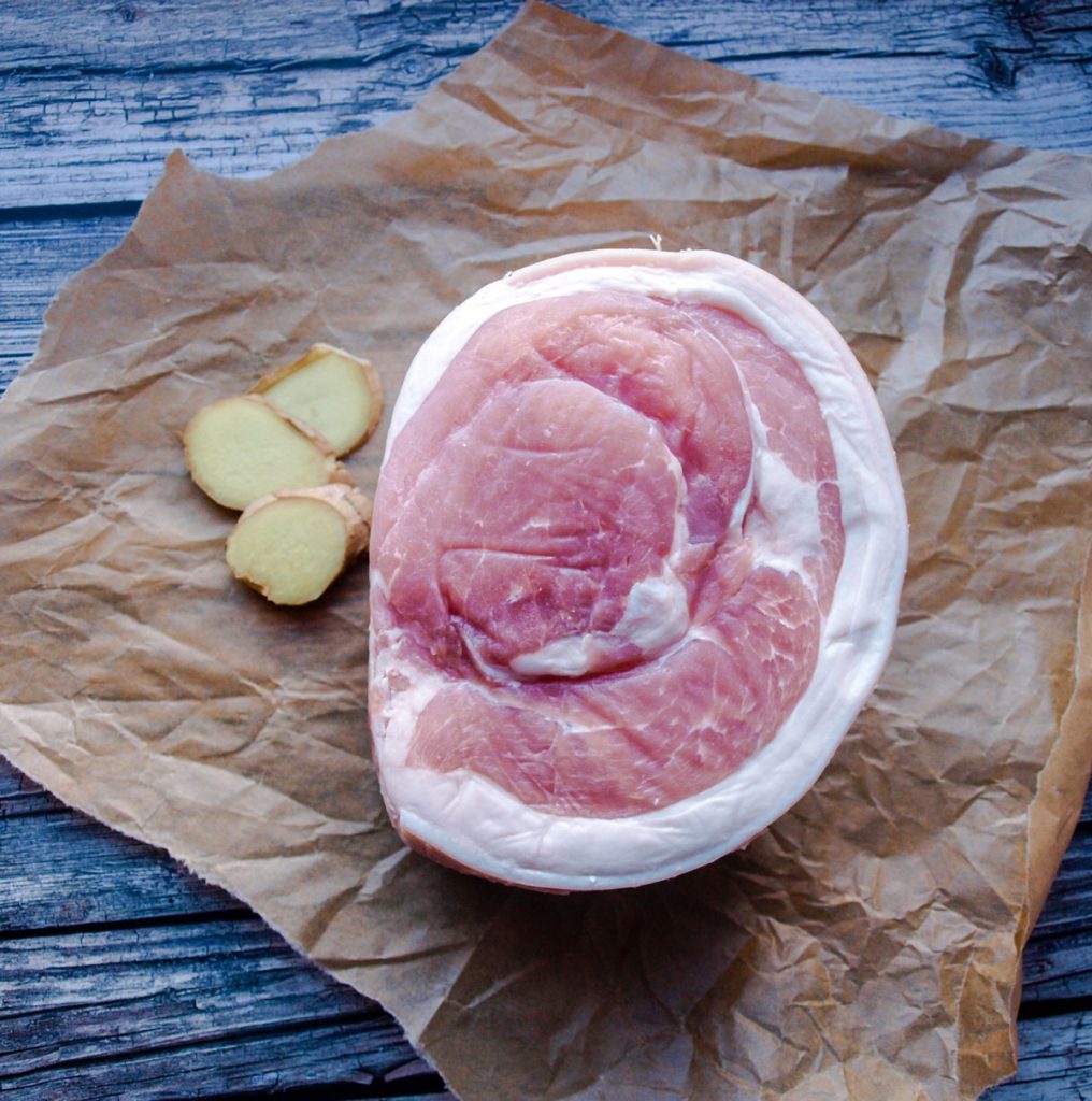 Raw ham or gammon joint on brown paper with fresh ginger.