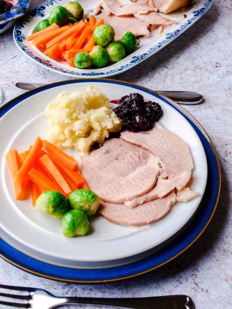 Slow Cooker Ham in Ginger Beer on plate with carrots, brussels sprouts, mashed potato and Cranberry & Red Wine Sauce
