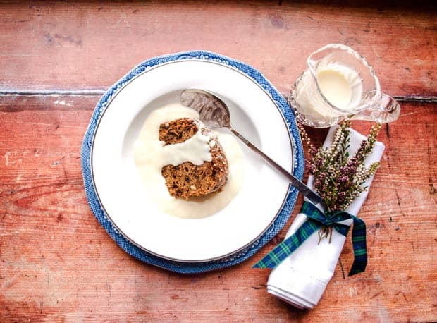 Bowl of fruit pudding with custard and napkin with heather. Jug of custard