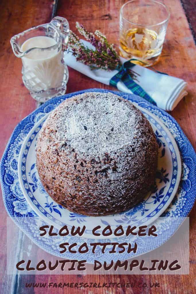 Large steamed fruit pudding on blue plate with jug of custad and napkin with heather - text reads Slow Cooker Scottish Cloute Dumpling.