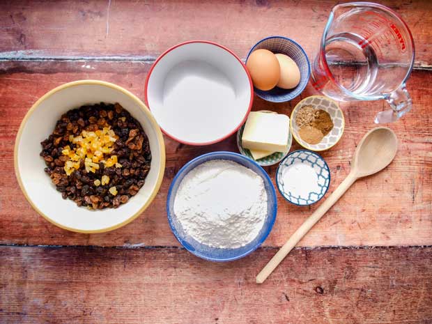 Bowls of dried fruit, flour, sugar, eggs butter and spices, wooden spoon and jug