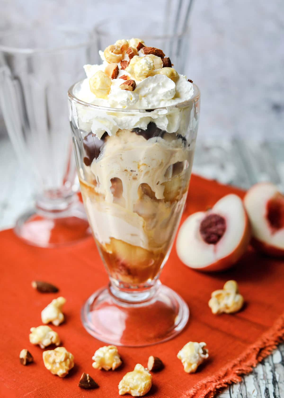 Salted Caramel Peach Ice Cream Sundae in tall glass with peaches and popcorn 