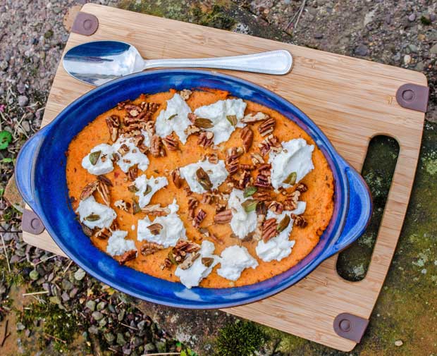 Sweet Potato mash with ricotta sage and pecans in a blue serving dish on a wooden board with a spoon.