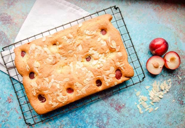 Plum and Almond Cake on cooling tray with fresh plums and flaked almonds.