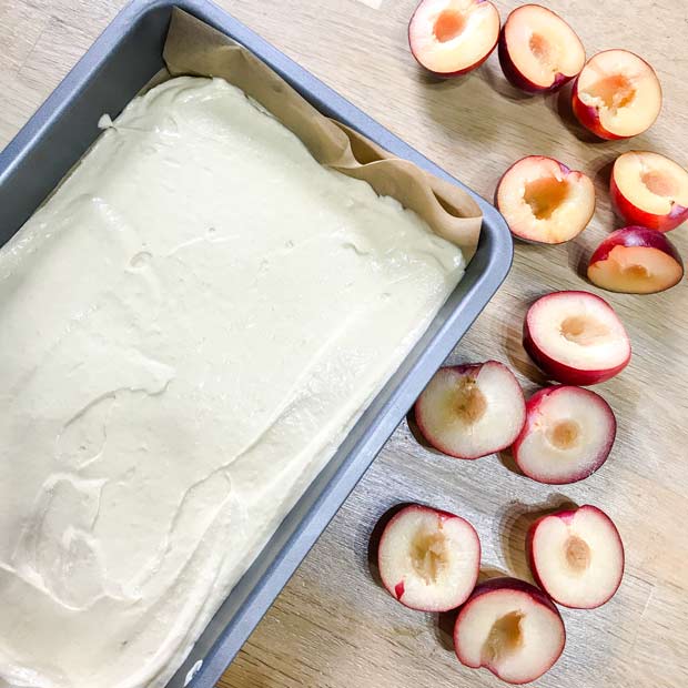 Baking pan with cake mix in it and halved plums