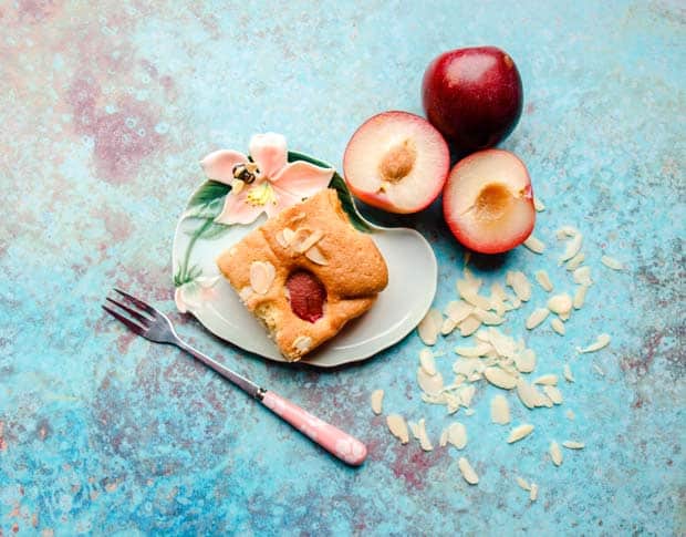 Square of Plum and Almond Cake on a small decorated plate withplums and almonds and a cake fork.