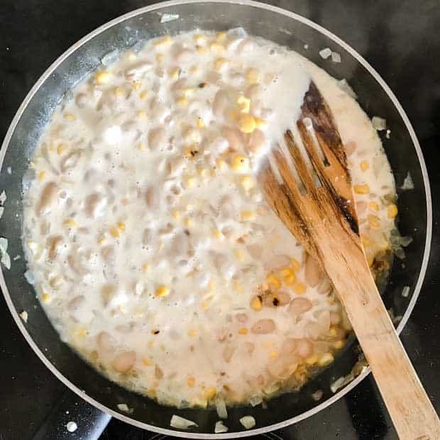 Frying pan with wooden spatula, corn and cream.