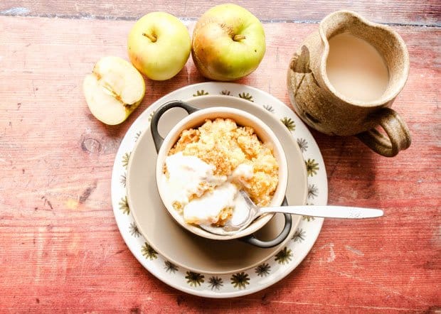 Bowl of apple crumble dessert with apples and jug of custard