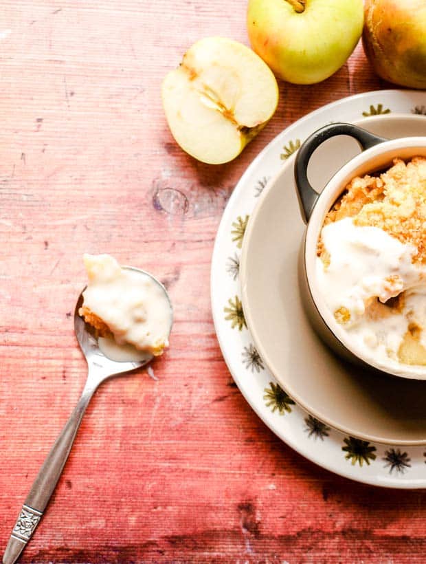 Spoon of Classic Apple Crumble with half of bowl and apple showing.