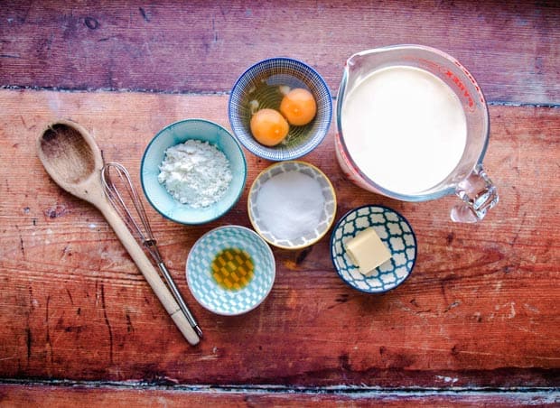 jug with milk, bowls with eggs, flour, sugar, butter and vanilla extract wooden spoon