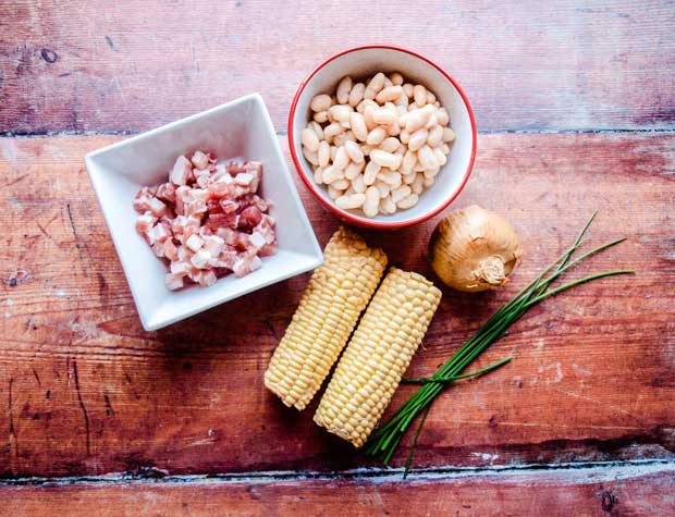 corn on the cob, bacon pieces, onion and white beans in a bowl