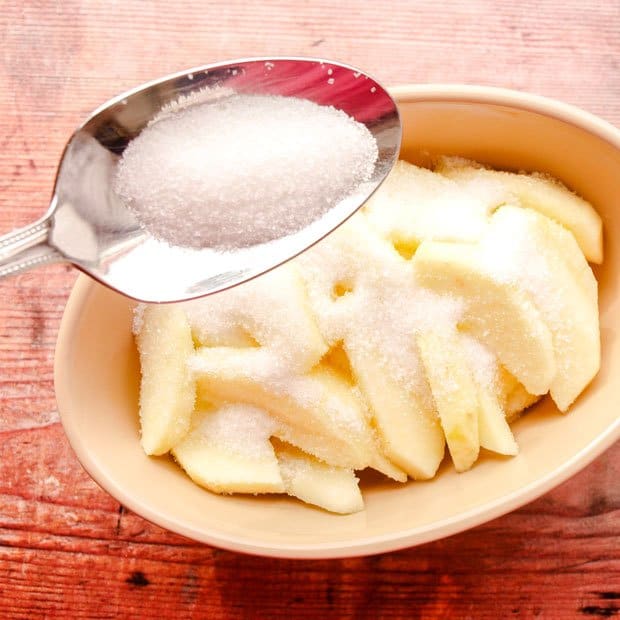 Baking dish with apples and a spoon with sugar