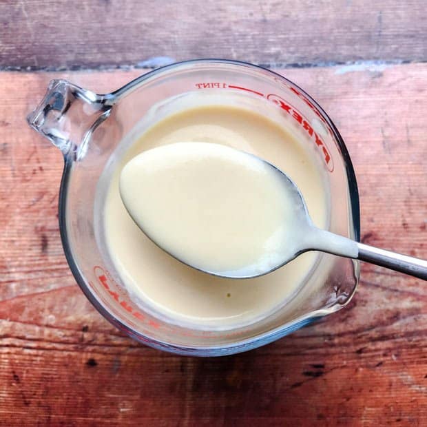 Spoonful of Easy Vanilla Custard Sauce over a jug