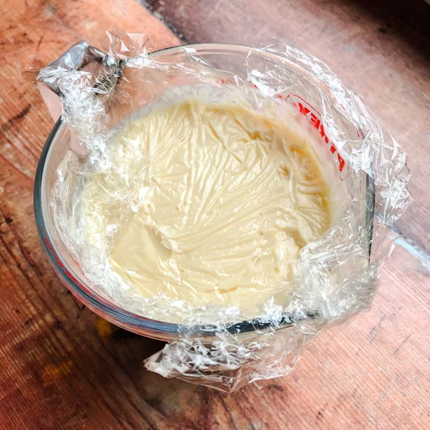 Jug of custard covered with plastic wrap.