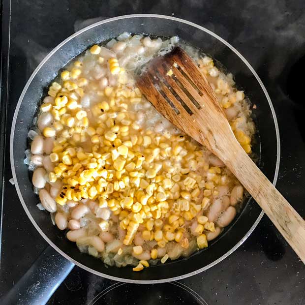 Frying pan with beans and sweetcorn. Wooden spatula.