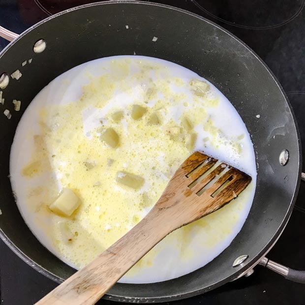 Pan with milk and cooked potatoes. Wooden spatula.