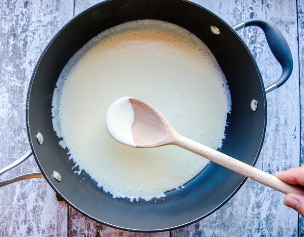 Pan with thick milk and potato liquid and wooden spoon.