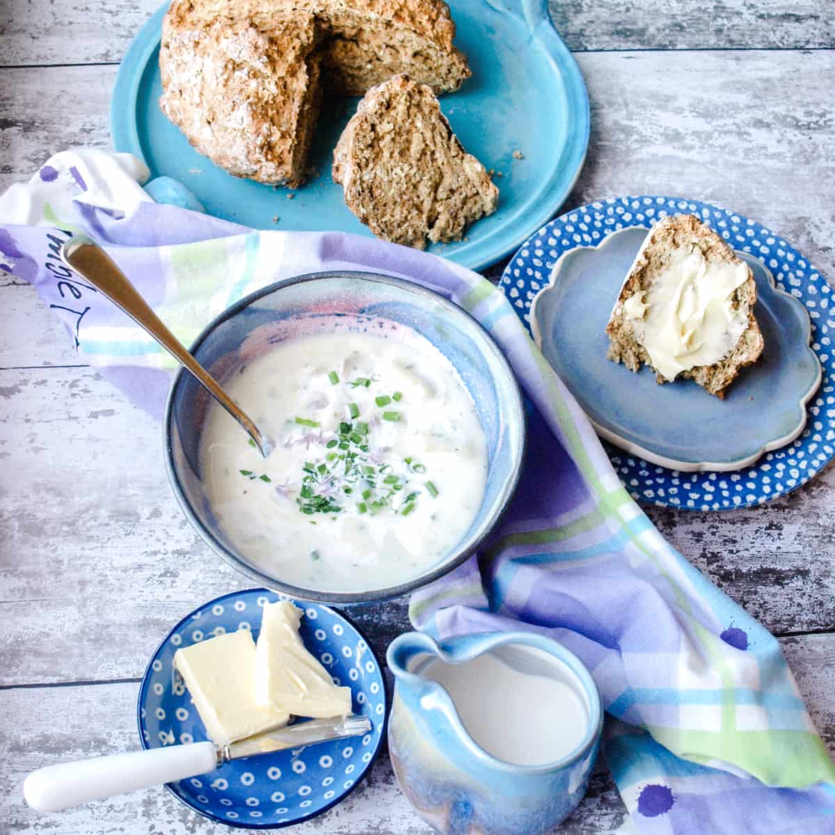 Bowl of Cullen Skink with spoon in it, soda bread, butter and jug of cream.