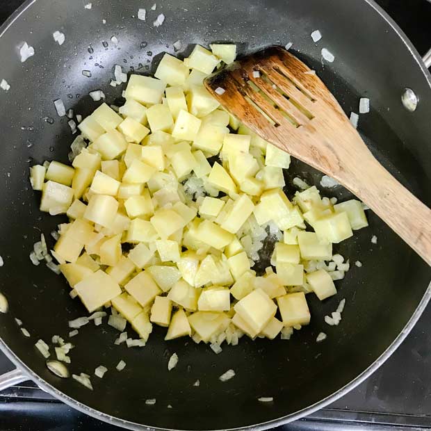 Pan with potato cubes and diced onion. Wooden spatula