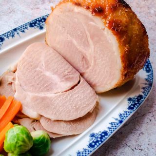 Slow Cooker Ham in Ginger Beer - Ham on platter with slices cut, brussels sprouts and carrots