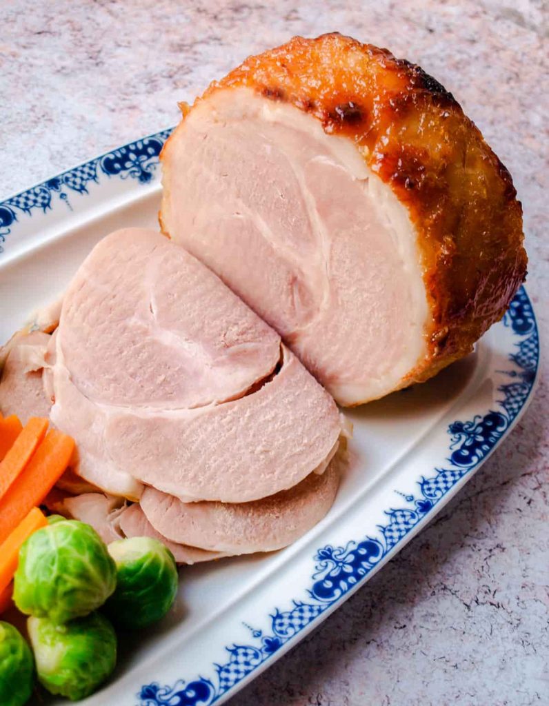 Slow Cooker Ham in Ginger Beer - Ham on platter with slices cut, brussels sprouts and carrots