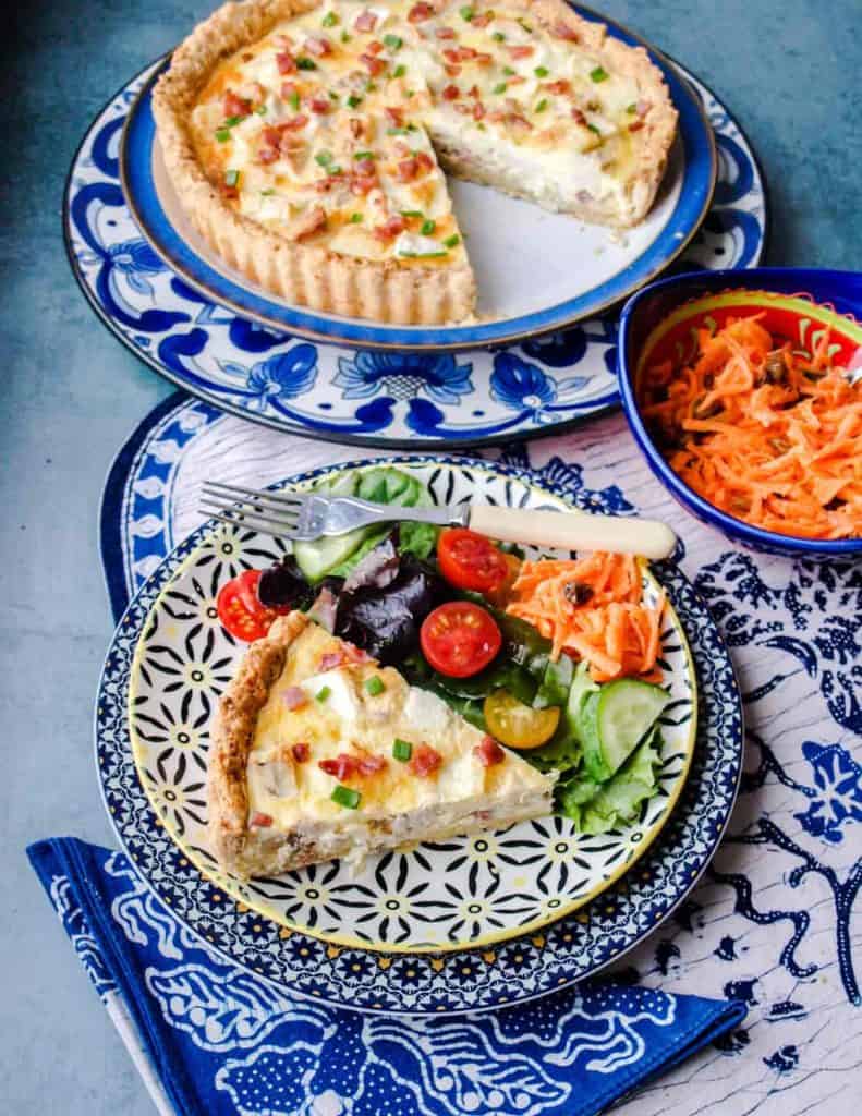 Large quiche with slice cut out. Slice of quiche on plate with salad
