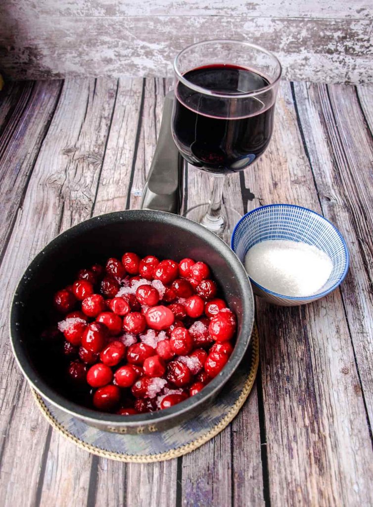 pan of cranberries, glass of red wine, bowl of white sugar.