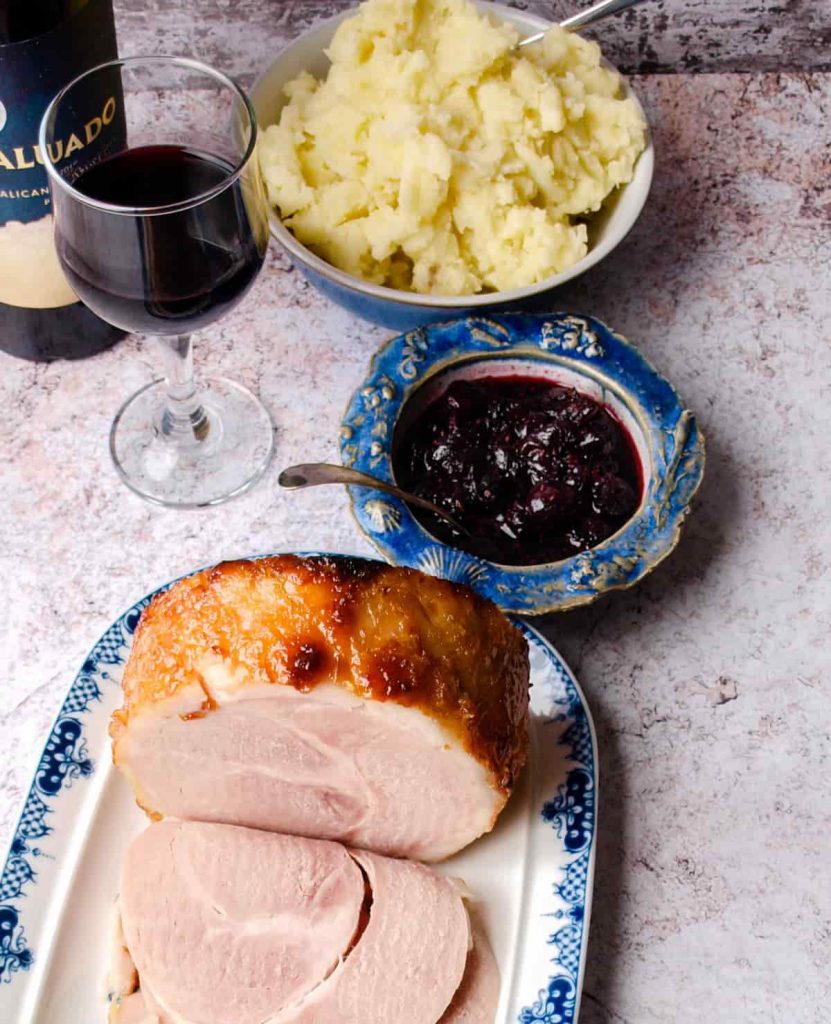 Cooked Ham with mashed potatoes in bowl, Cranberry & Red Wine Sauce in bowl, glass of wine and bottle.