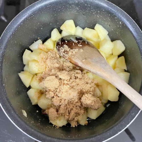 Apples and sugar in pan with wooden spoon