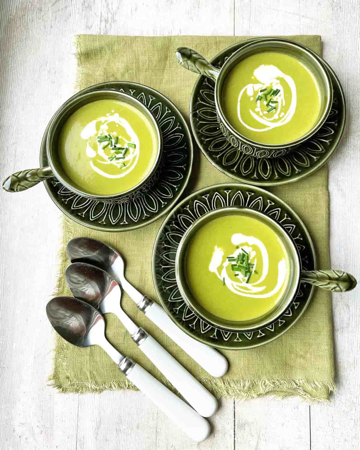 three bowls of lettuce soup with spoons