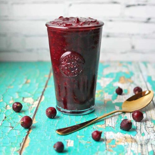 jar of blackcurrant compote with spoon and blackcurrants.