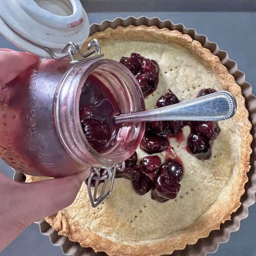 cherry and almond frangipane tart spoon cherries into pastry case.