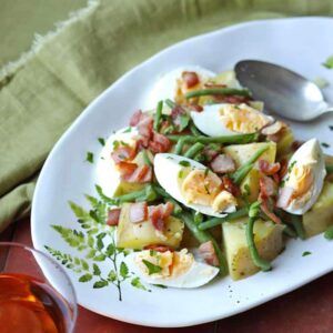 french bean and potato salad with egg and bacon on platter with spoon.