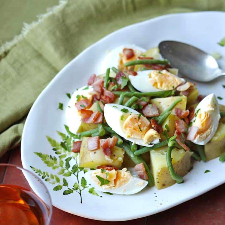 french bean and potato salad with egg and bacon on platter with spoon.